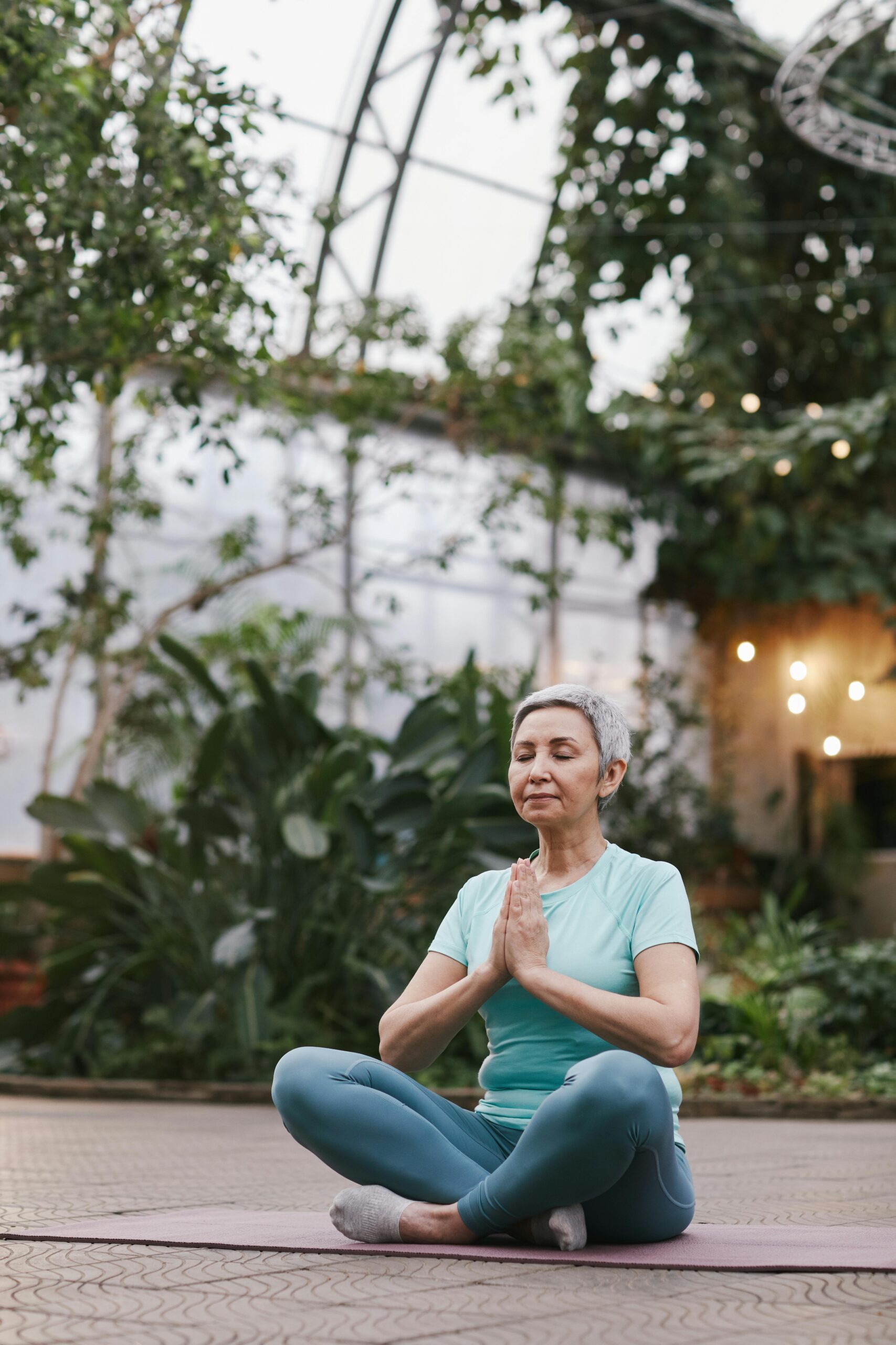 Senior woman practicing yoga meditation in a serene botanical garden, promoting wellness and relaxation.